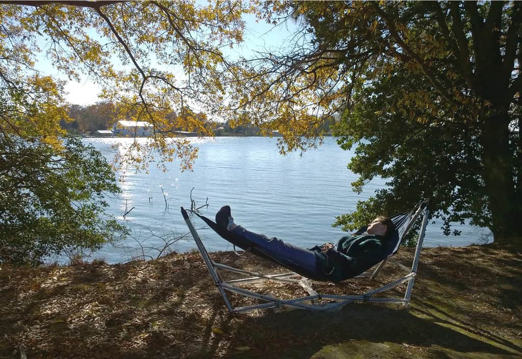 a man lying in a hammock by a lake. Nature therapy is emerging as a powerful antidote to stress